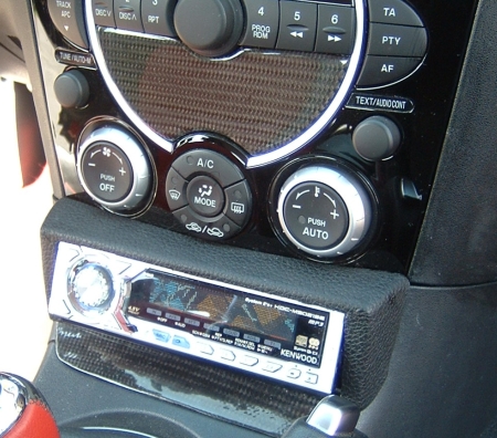 Mazda RX-8 középkonzol alá került a Kenwood fejegység, amely egyedi bőrözött takarópanelt kapott, Az installáció ma már a középkonzol dupla DIN nyílású csredarabjával is megoldható lenne.